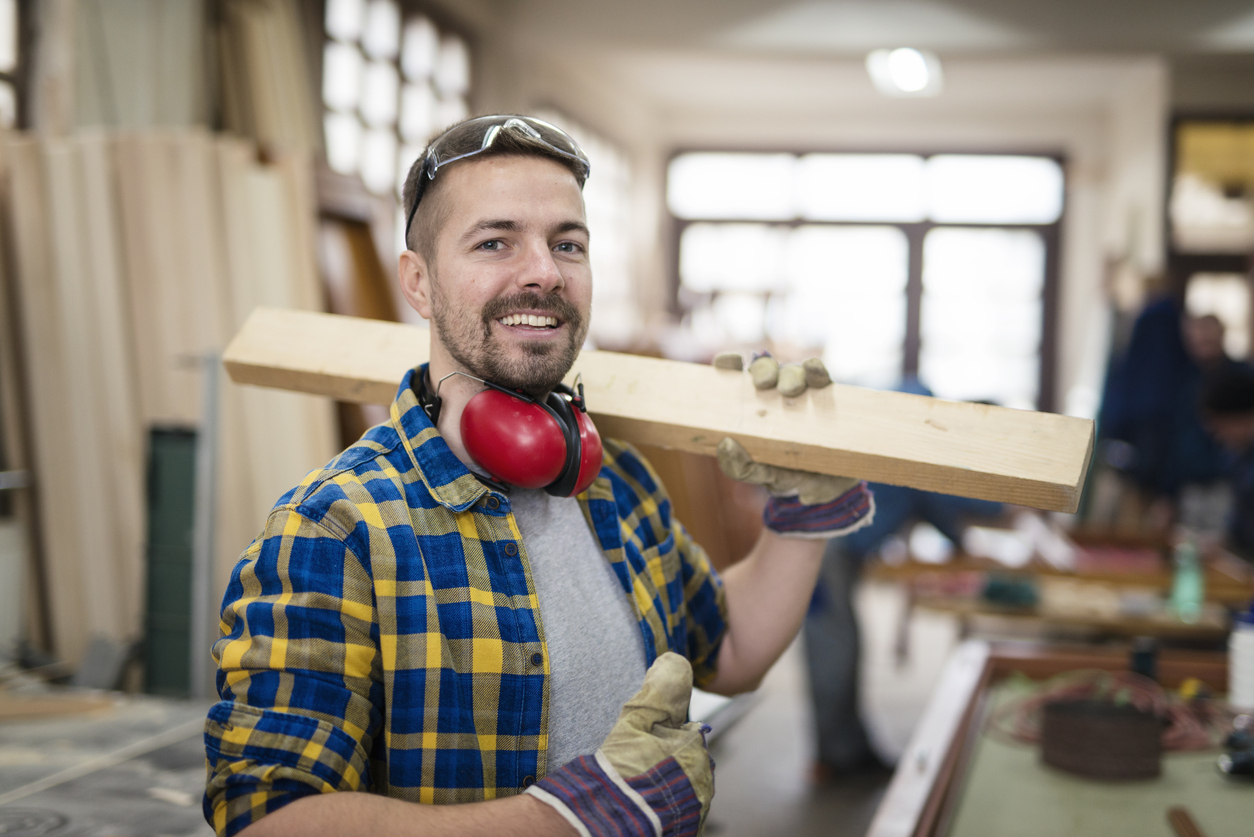 Un artisan portant une planche en bois avec le sourire